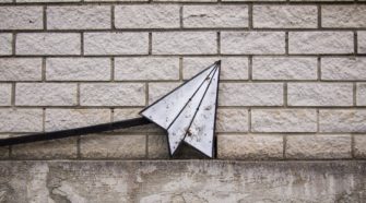 Papierflieger-Icon aus Metall lehnt an Wand