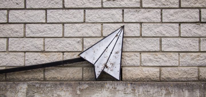 Papierflieger-Icon aus Metall lehnt an Wand