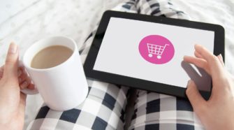 Studie zu Reimagining Commerce: Frau in karierter Hose hält Kaffee-Tasse und Tablet auf dem Schoß für Onlineshopping & Einkaufsgewohnheiten
