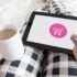 Studie zu Reimagining Commerce: Frau in karierter Hose hält Kaffee-Tasse und Tablet auf dem Schoß für Onlineshopping & Einkaufsgewohnheiten