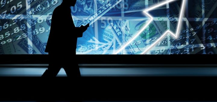 Geschäftsmann vor riesigem Monitor mit Zahlen und Grafen, die Richtung Erfolg weisen