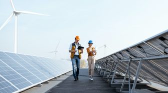View on the rooftop solar power plant with two engineers walking and examining photovoltaic panels. Concept of alternative energy and its service