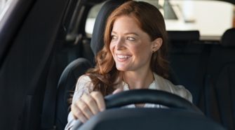 Mature beautiful woman sitting in car looking away while trying new automobile. Portrait of daydreaming mature woman doing drive test of new car. Cheerful smiling lady enjoying driving while looking away.